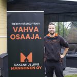 Rakennusliike Mannonen Oy:n toimitusjohtaja Joona Mannonen seisoo keltaisen talon ja mustan terassin edustalla. Vieressä roll-up, jossa teksti "Vahva osaaja".